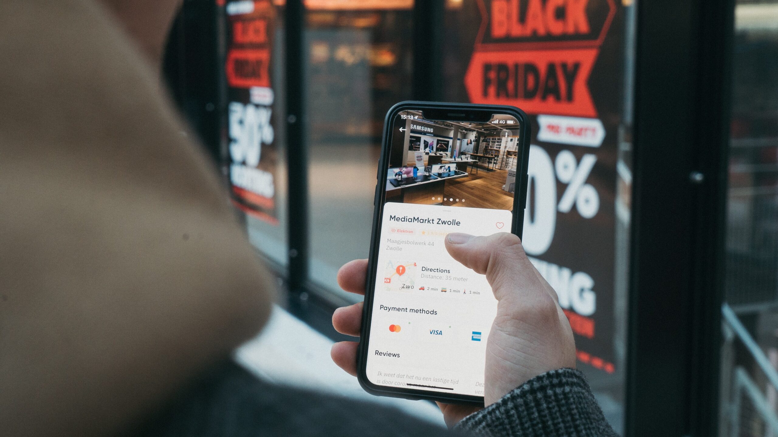 Image of person looking at a phone on black Friday. Storefront in the background with posters of sales.